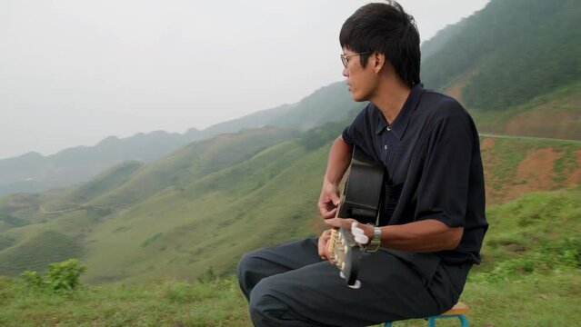 cinematic video of a young korean man sat on the top of a high cliff getting some headspace and playing his guitar for no one but himself.
