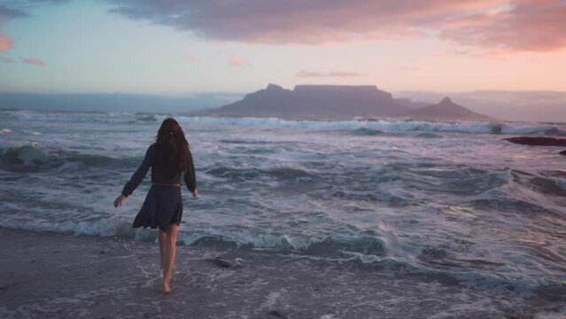 slow motion video of a woman running into the sea and dancing in the extremely wavy water just as the sun goes down while camping on the beach.