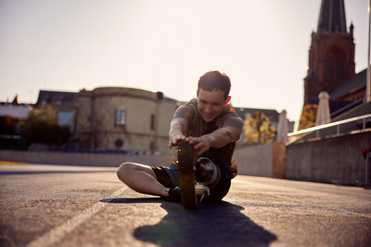 Smiling man with a prosthetic blade stretching on a running track