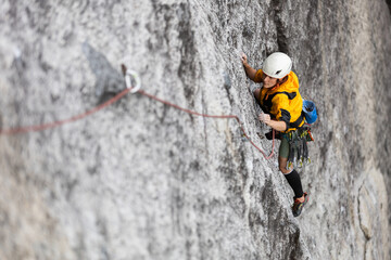 Fototapeta premium Person climbing in high mountains with yellow jacket rope and helmet in nature, confidence and risk, safety