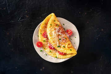 An omelet with tomato and parsley, eggs for breakfast, a healthy vegetarian omelette with cheese, overhead flat lay shot on a black slate background