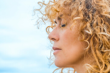 Close up side portrait of pretty adult woman with closed eyes and blonde natural healthy curly long...