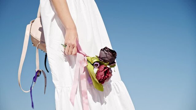 Girl in white dress holding a bouquet of flowers against the sky