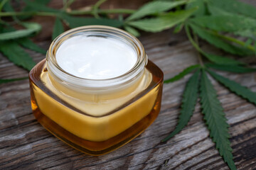 Cosmetic cream for skin care from hemp. Natural cosmetics. Moisturizing cream in jar with hemp leaves on wooden background.