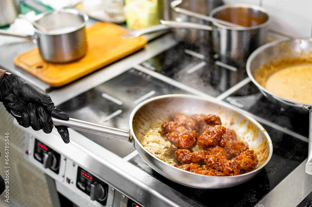 Wall mural woman chef cooking chicken wings in a sauce on pan in the kitchen