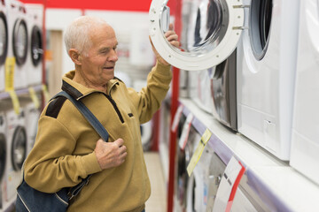 Elderly man looks at the washing machine on the counter