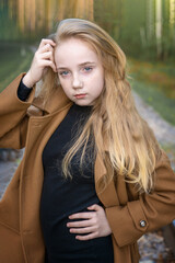 Naklejka premium Close-up portrait of a romantic 13-15 year old girl in the woods. A girl with long blond hair looks at the camera
