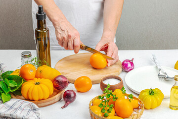 A woman is preparing a tomato salad. Ripe vegetables, herbs, aromatic spices, olive oil