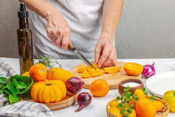 A woman is preparing a tomato salad. Ripe vegetables, herbs, aromatic spices, olive oil