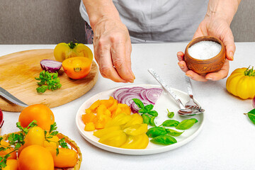 A woman is preparing a tomato salad. Ripe vegetables, herbs, aromatic spices, olive oil