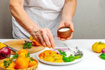 A woman is preparing a tomato salad. Ripe vegetables, herbs, aromatic spices, olive oil