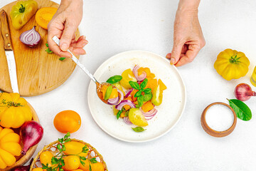 A woman is preparing a tomato salad. Ripe vegetables, herbs, aromatic spices, olive oil