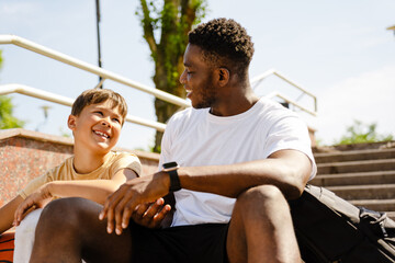 African man talking with his son while sitting outdoors after basketball training