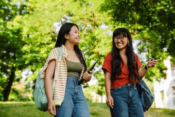 Two cheerful asian women walking together in park