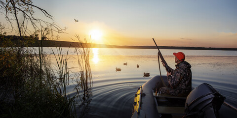 Duck hunter at sunrise. Waterfowl hunter in boat at sunset. banner with copy space.