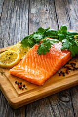 Fresh raw salmon steak with salt and fresh vegetables on wooden background