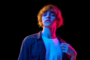 Portrait of young man in casual clothes posing against black studio background in neon lights. Concept of human emotions, facial expression, youth, lifestyle, casual fashion. Ad