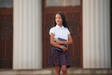 Conception of knowledge. School girl in uniform is outdoors near the building