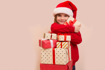 Happy child girl in Santa red hat holding Christmas presents on a beige background. Christmas time. banner. copy space
