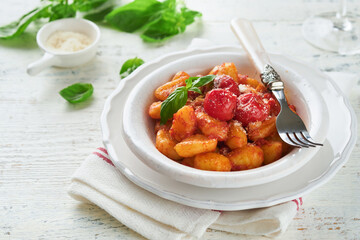 Potato gnocchi. Traditional homemade potato gnocchi with tomato sauce, basil and parmesan cheese on kitchen table on light grey kitchen table background. Traditional Italian food. Top view.