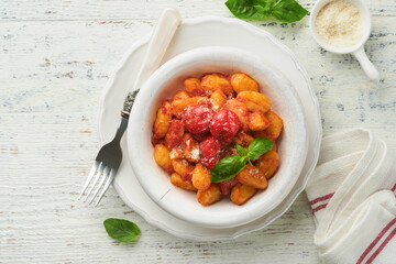 Potato gnocchi. Traditional homemade potato gnocchi with tomato sauce, basil and parmesan cheese on kitchen table on light grey kitchen table background. Traditional Italian food. Top view.