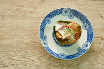steamed chop snakehead fish with curry dressing coconut milk and topping slice lemon grass leaf in banana leaf tray on plate