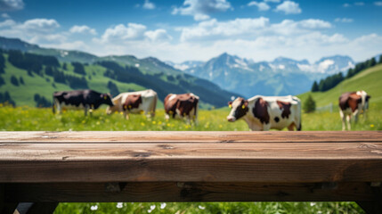 Naklejka premium Empty wooden tabletop for product background and montage, Adipian meadow with herd of cows, banner mockup and dairy product advertisement with beautiful mountains alpine meadow behind