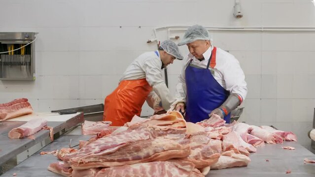 Butchers men cutting pork meat from bones for preparing delicacies in meat shop. Selected meat products in butchery, meat factory. Industrial food plant, preparation raw for production. Food industry.