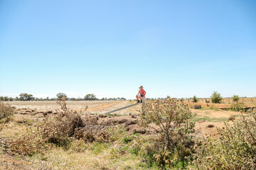 Boy sitting on farm fence in dry summer conditions
