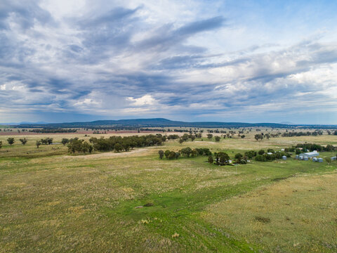 Aerial view of lightly overcast sky with farm paddock and homestead with sheds below