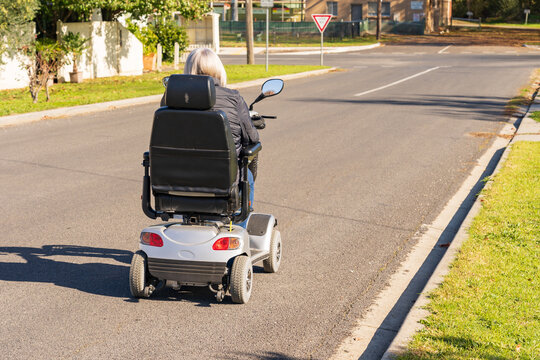 Rear view of an elderly lady riding a mobility scooter down a road