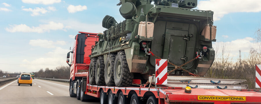 Back view armoured personnel carrier stryker with air defense system trailer hauler carrier truck drive military convoy highway road. US troops moving reloceation force reinforcement eastern Europe