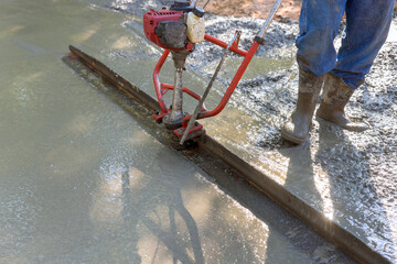 Tamping machine is used to align fresh concrete compacted layer in new driveway that is being constructed