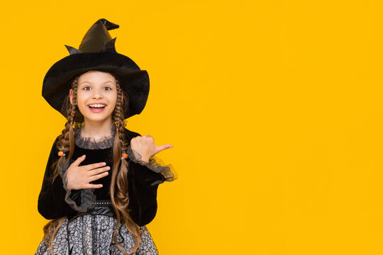 Portrait of a beautiful young witch pointing her finger to the side at an advertisement, looking into an empty space, A Sorceress in a Halloween costume on an isolated yellow background.