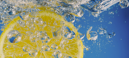 Underwater lemon slice in soda water or lemonade with bubbles. Refreshing soda tonic fizzy cocktail. Close up of lemons and ice cubes in glass. Lime in splashing sparkling water cold drink beverage.