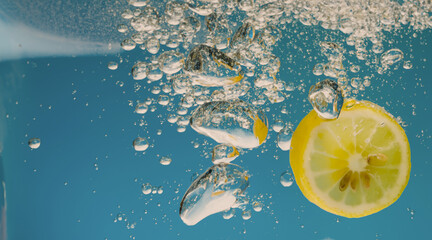 Underwater lemon slice in soda water or lemonade with bubbles. Refreshing soda tonic fizzy cocktail. Close up of lemons and ice cubes in glass. Lime in splashing sparkling water cold drink beverage.