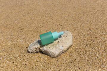 Fototapeta na wymiar Emerald bottle of serum for skin care on the beach. Stylish concept of cosmetics and body care