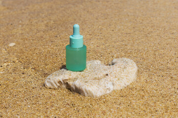 Fototapeta na wymiar Natural serum for face and skin in a frosted glass bottle. Stylish concept of care cosmetics on a sandy beach