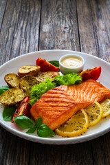 Seared salmon steak with baked potatoes and fresh vegetable salad served on wooden table

