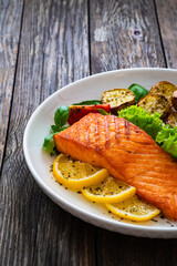 Seared salmon steak with baked potatoes and fresh vegetable salad served on wooden table
