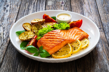 Seared salmon steak with baked potatoes and fresh vegetable salad served on wooden table
