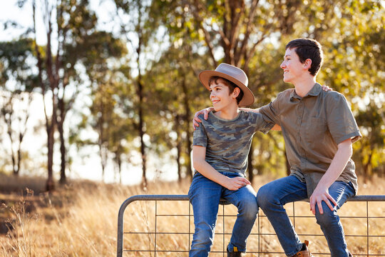 Smiling brothers with hands on each others shoulders together on gate in country