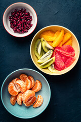 Bowls with fresh fruits (grapefruits,  tangerines, orangespomegranate seeds,  and kiwi), preparing fruit salad, ingredients