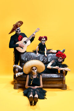 Halloween Family. Happy father, mother and children girls in halloween mexico costume and makeup. Crazy skeleton faces on yellow studio background