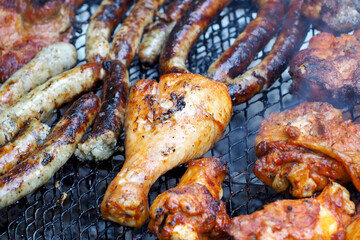 Chicken legs in spices and sausages are cooked on a grill grid. outdoor barbecue. cooking meat dishes