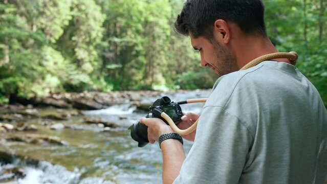 Smiling man taking picture of mountain river on camera in forest 
