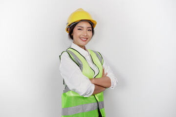 Smiling Asian woman labor worker in industry factory, posing with arms folded, wearing yellow safety helmet, green vest and uniform, isolated white background.