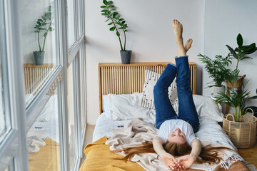 Pretty happy red-haired woman sitting on the bed. Portrait of smiling woman posing in bright home...