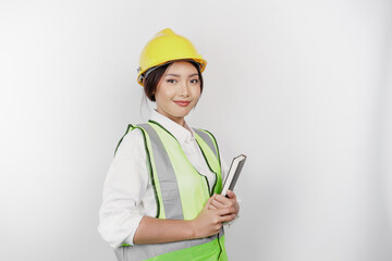 A smiling Asian woman labor wearing safety helmet and vest, holding her book, isolated by white background. Labor's day concept.