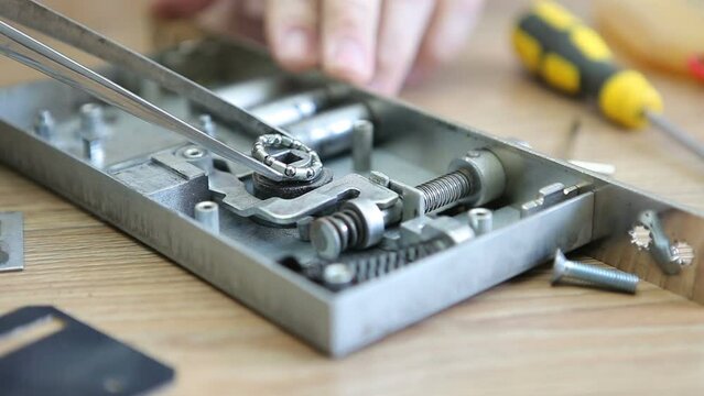 A man disassembles and repairs an internal door lock, removes the bearing with tweezers. Macro photography.